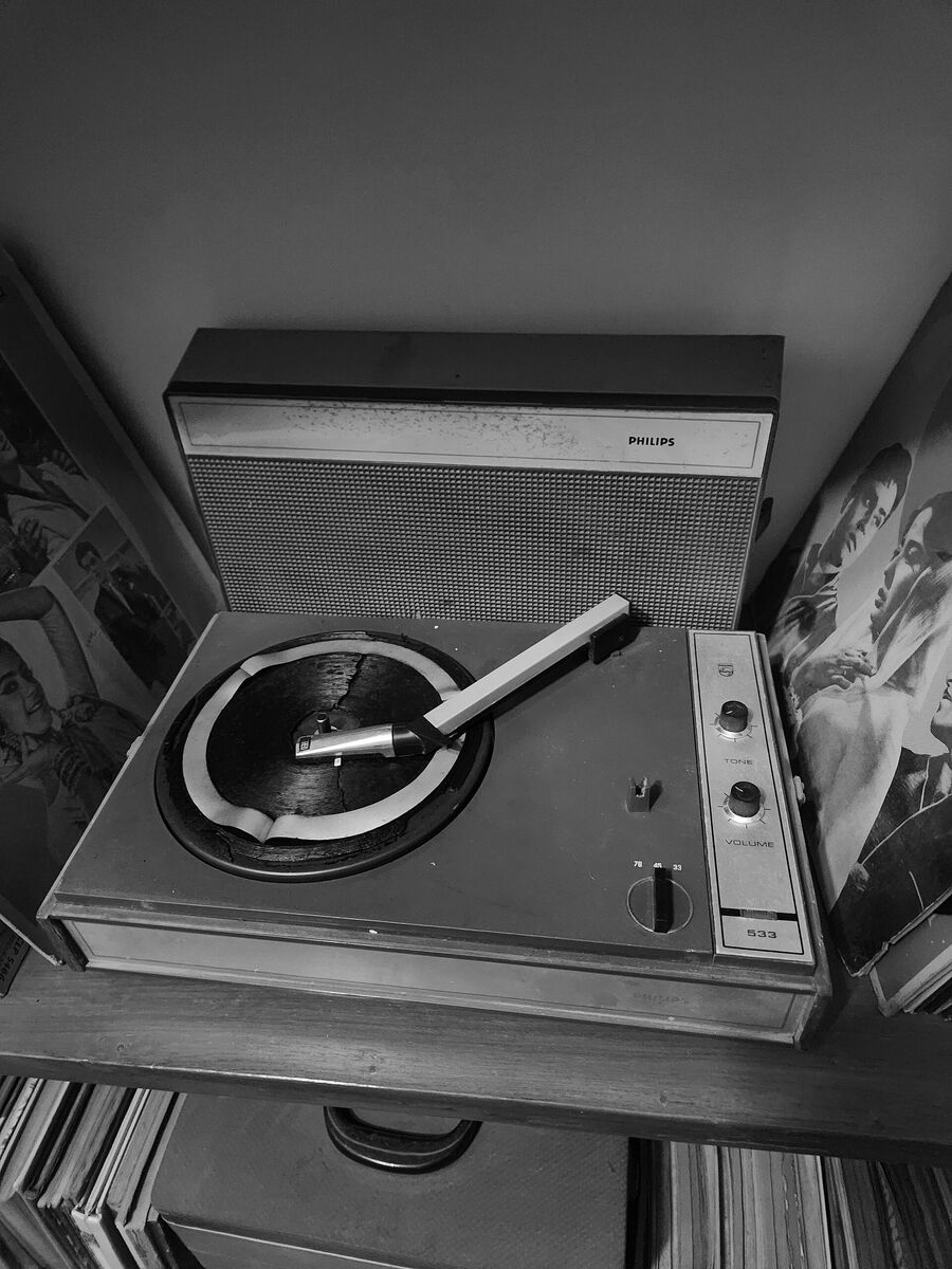 Un tocadiscos portátil gris con un disco puesto, en un estante